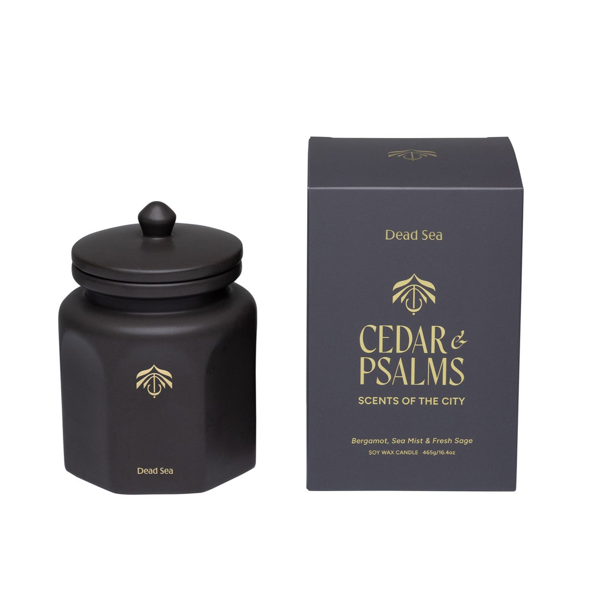 A matte black candle vessel with a matching lid next to its black packaging box, both featuring gold lettering that reads 'Dead Sea' and 'CEDAR & PSALMS SCENTS OF THE CITY'.