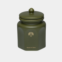 An olive green hexagonal ceramic candle vessel with a matching lid, featuring a gold logo and the text 'Mount of Olives' on the front, set against a light gray background.