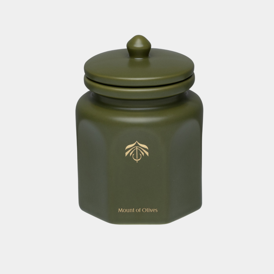 An olive green hexagonal ceramic candle vessel with a matching lid, featuring a gold logo and the text 'Mount of Olives' on the front, set against a light gray background.