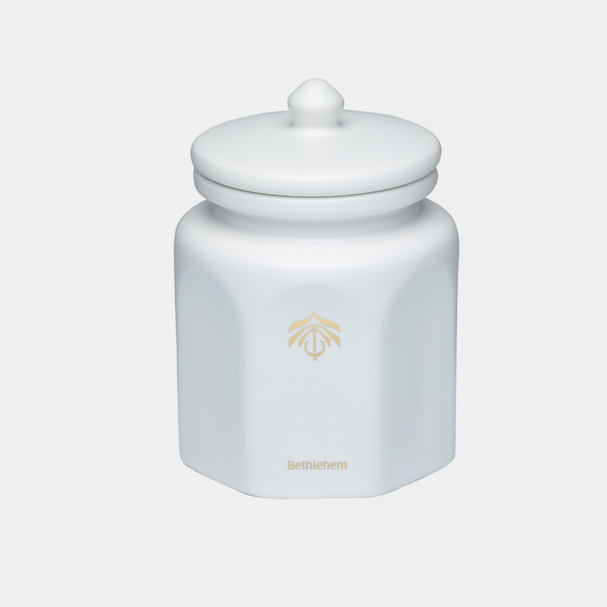 A white hexagonal ceramic candle vessel with a matching lid and a small gold printed logo and the word 'Bethlehem' on the front, set against a light gray background.