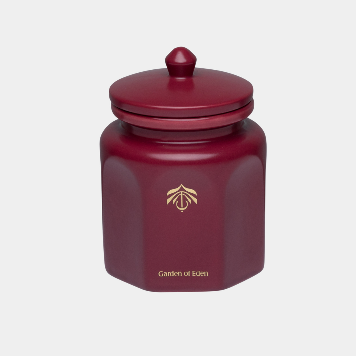 A dark red hexagonal candle vessel with a matching lid, featuring a gold logo and the text 'Garden of Eden' on the front, set against a light gray background.