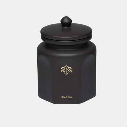 A matte black hexagonal cande vessel with a matching lid and a small gold logo and 'Dead Sea' text on the front, set against a light gray background.